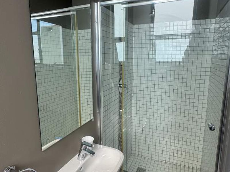 A modern bathroom featuring a wall-mounted basin, a glass-enclosed shower with mosaic tile accents, and neutral floor tiling.