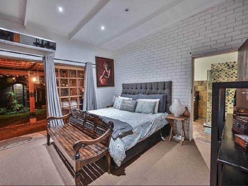 Spacious bedroom featuring an exposed brick feature wall, exposed beam ceiling, split-system air conditioning, and direct access to an en-suite bathroom and outdoor area.