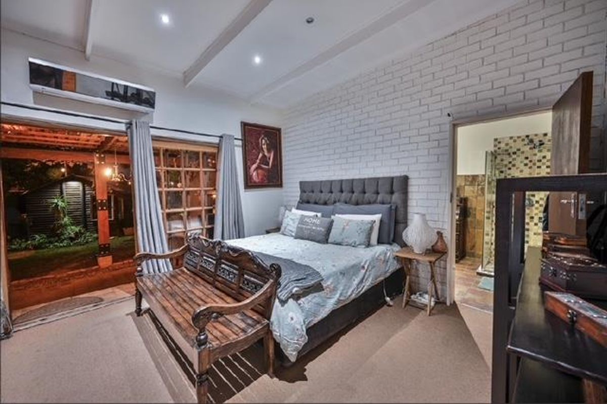 Spacious bedroom featuring an exposed brick feature wall, exposed beam ceiling, split-system air conditioning, and direct access to an en-suite bathroom and outdoor area.