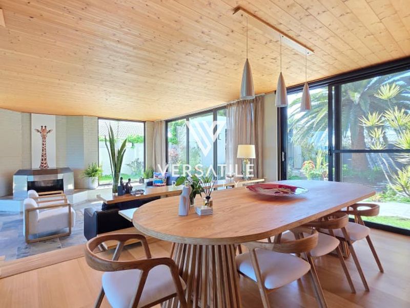 Spacious open-plan living and dining area featuring a warm timber-clad ceiling, large sliding glass doors, and a built-in fireplace with stone flooring.