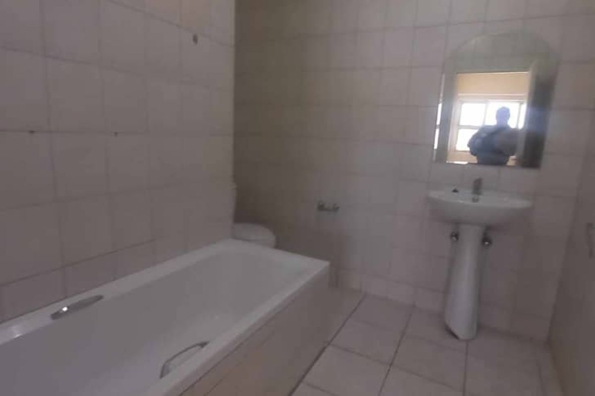 A dated bathroom featuring a standard bathtub, pedestal basin, and full-height wall tiling, requiring cosmetic updates.