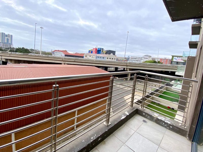 A balcony featuring a stainless steel balustrade and tiled flooring, offering an urban view of the surrounding infrastructure.
