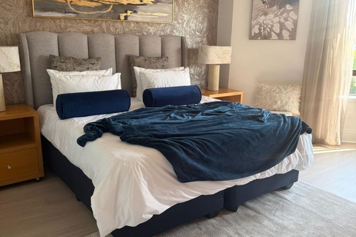 A well-maintained bedroom featuring light-toned laminate flooring, textured feature wallpaper, and neutral window treatments.