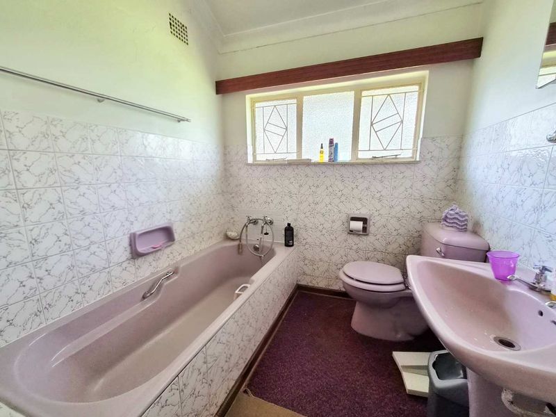 A dated bathroom featuring a vintage pink suite, tiled walls, and leaded glass windows, offering significant potential for a modern renovation.