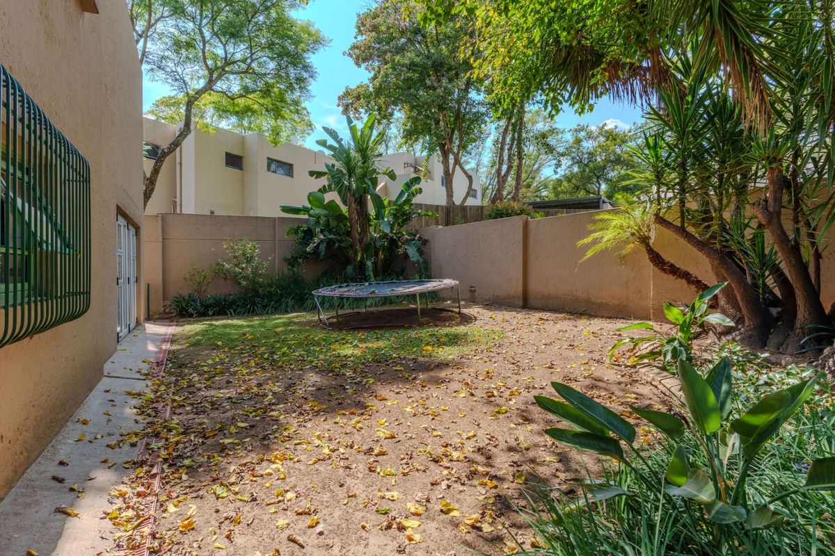 A private rear garden area featuring perimeter boundary walls, established trees, and a paved walkway adjacent to the townhouse structure.