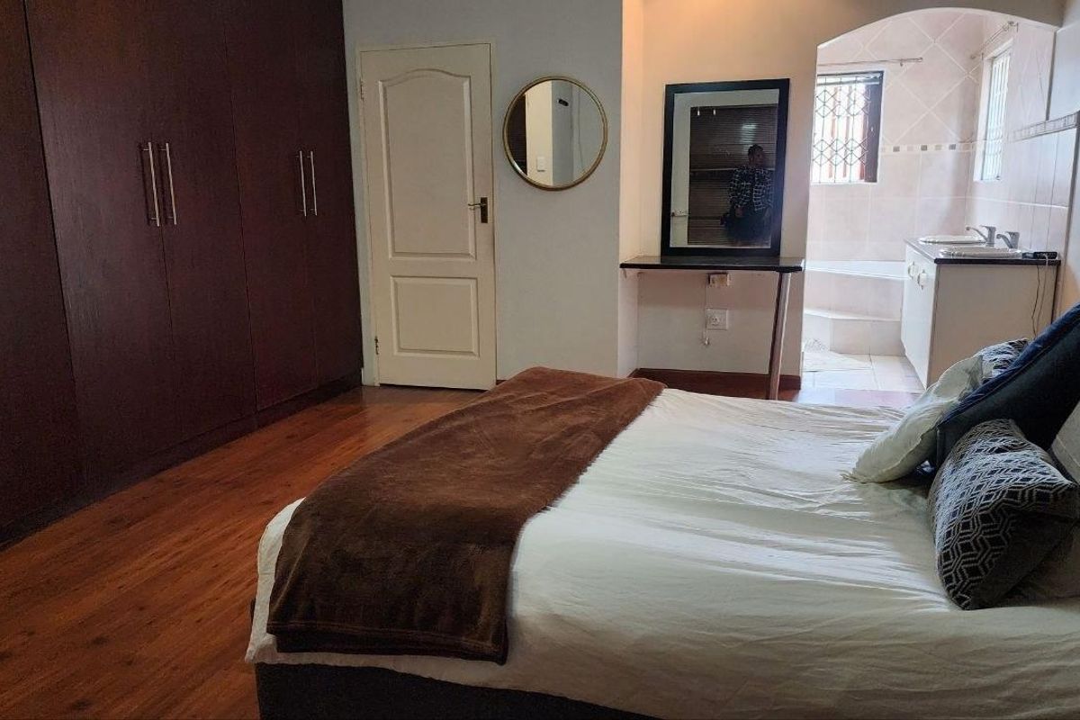 Spacious bedroom featuring extensive built-in wooden cabinetry, laminate flooring, and an en-suite bathroom area with a built-in vanity.