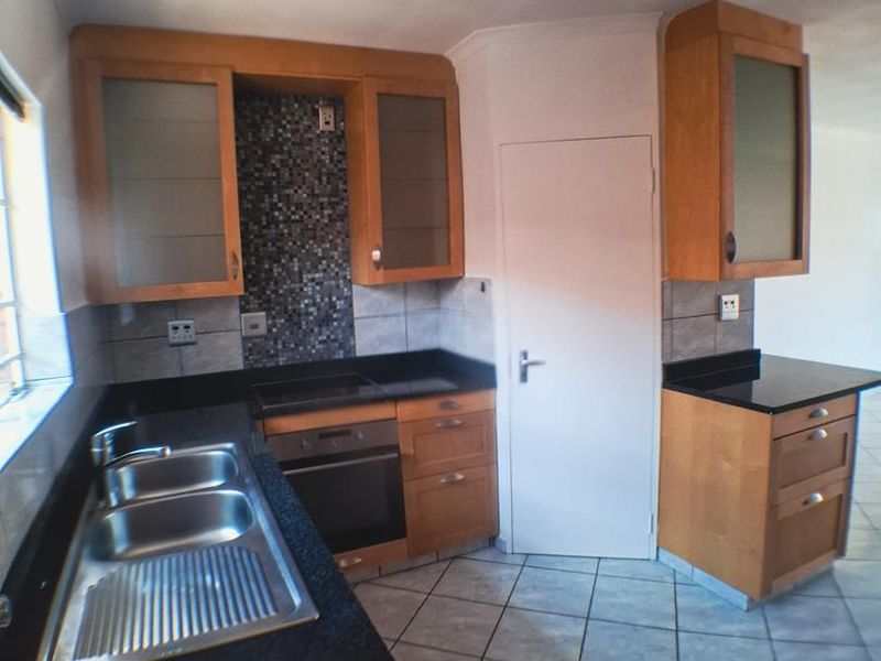 A functional kitchen featuring wooden cabinetry, granite countertops, a mosaic tile backsplash, and built-in appliances, finished with ceramic floor tiles.