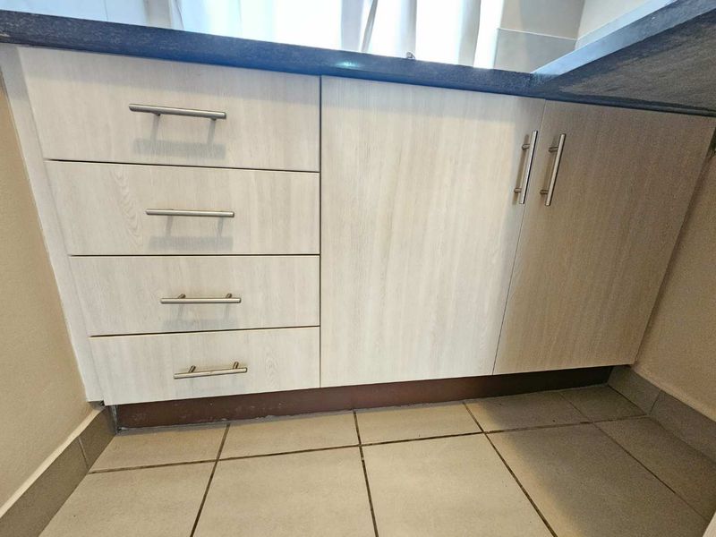 Close-up view of kitchen cabinetry featuring light wood-grain finish, stone countertops, and ceramic floor tiles.