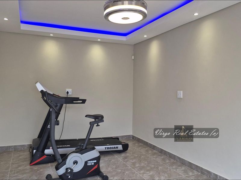 A modern, well-lit home gym featuring tiled flooring and decorative recessed ceiling lighting with integrated blue LED accents.