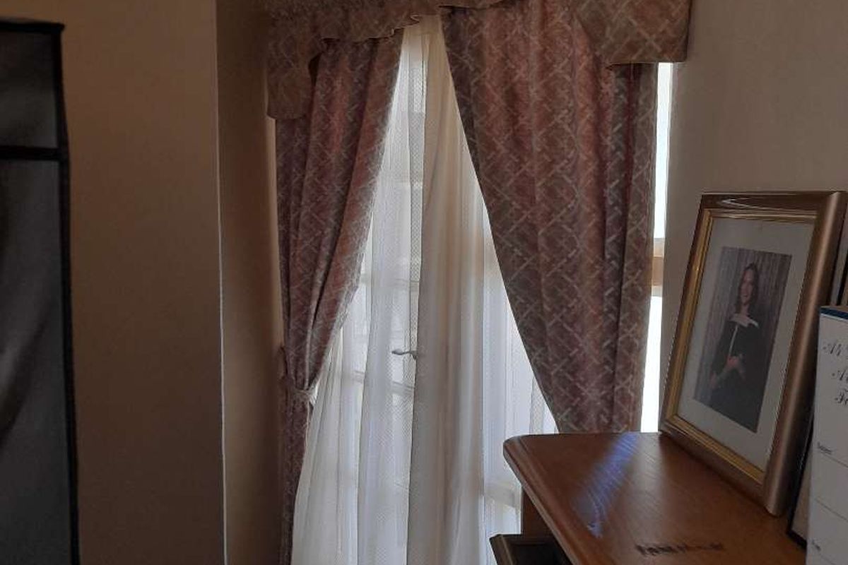 A bedroom corner featuring classic french doors with a decorative curtain pelmet and sheer drapes, providing natural light access.