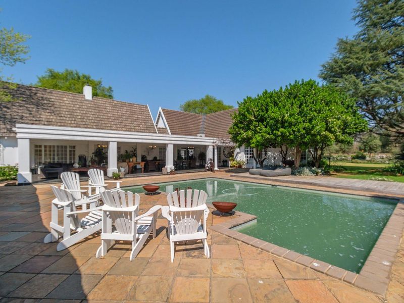 Spacious outdoor pool area featuring a large swimming pool, stone-paved patio, and a covered veranda overlooking the garden.
