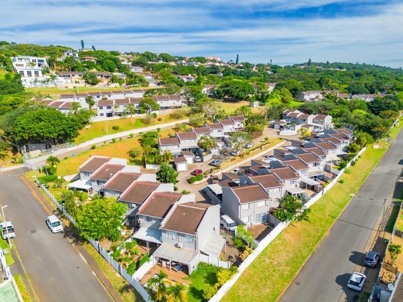 An aerial view of a residential townhouse complex featuring multiple units with tiled roofs, paved driveways, and established communal garden areas.
