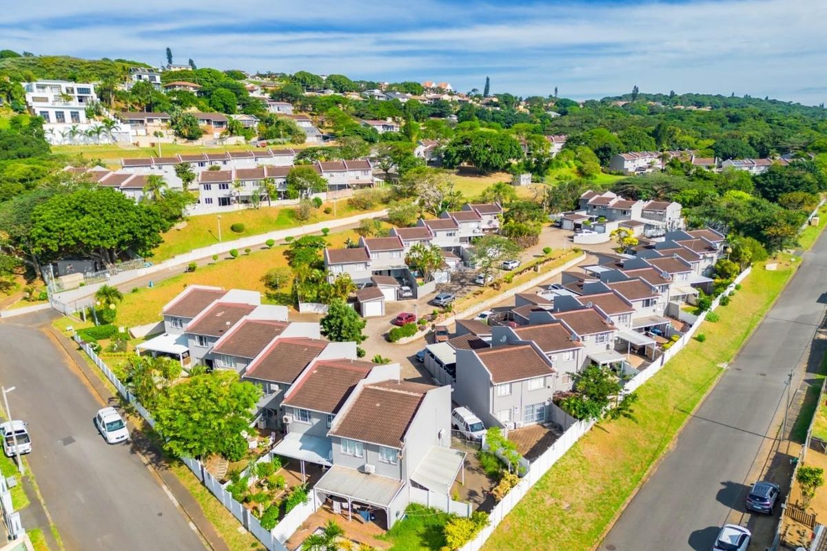An aerial view of a residential townhouse complex featuring multiple units with tiled roofs, paved driveways, and established communal garden areas.