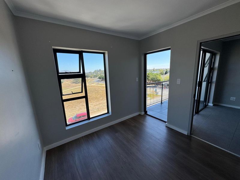 A bright, empty bedroom featuring modern laminate flooring, neutral walls, and direct access to a private balcony with scenic views.