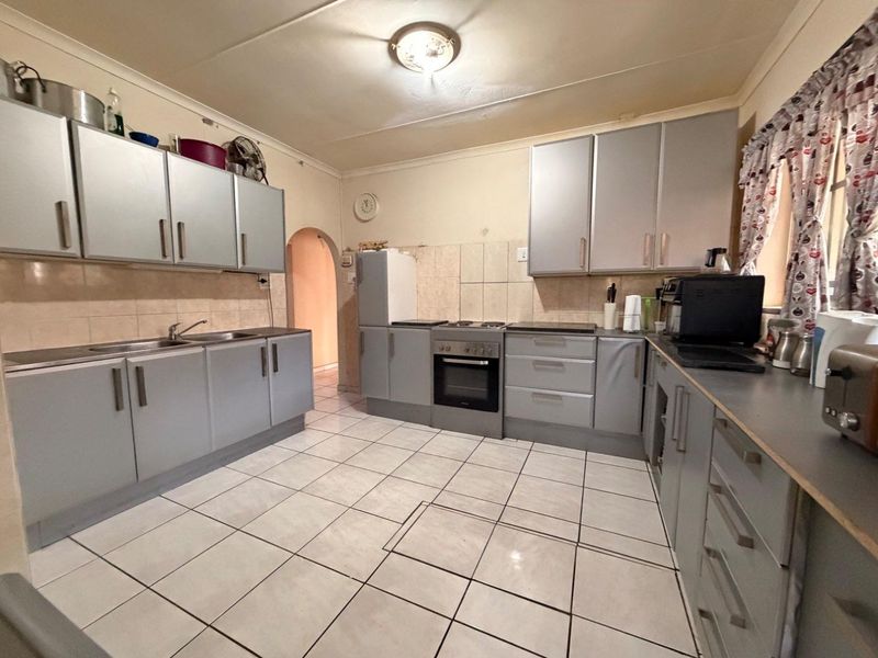 A functional kitchen featuring grey built-in cabinetry, a built-in oven with hob, tiled backsplash, and tiled flooring with an adjacent arched doorway.
