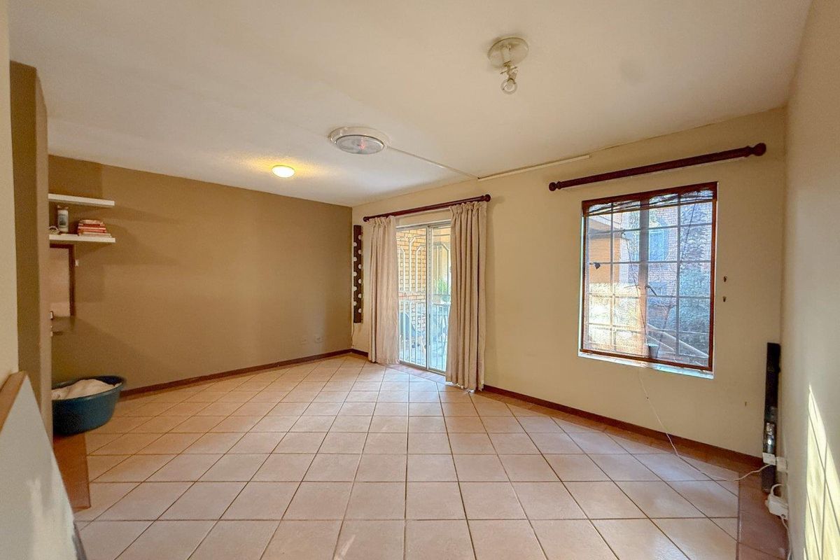 A spacious, empty living room featuring neutral tiled flooring, large windows, and a sliding glass door leading to an outdoor area.