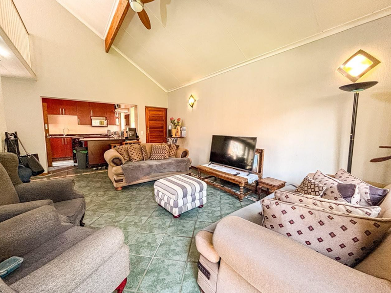 Spacious open-plan living area featuring a vaulted ceiling with exposed timber beams, tiled flooring, and an integrated kitchen with wooden cabinetry.