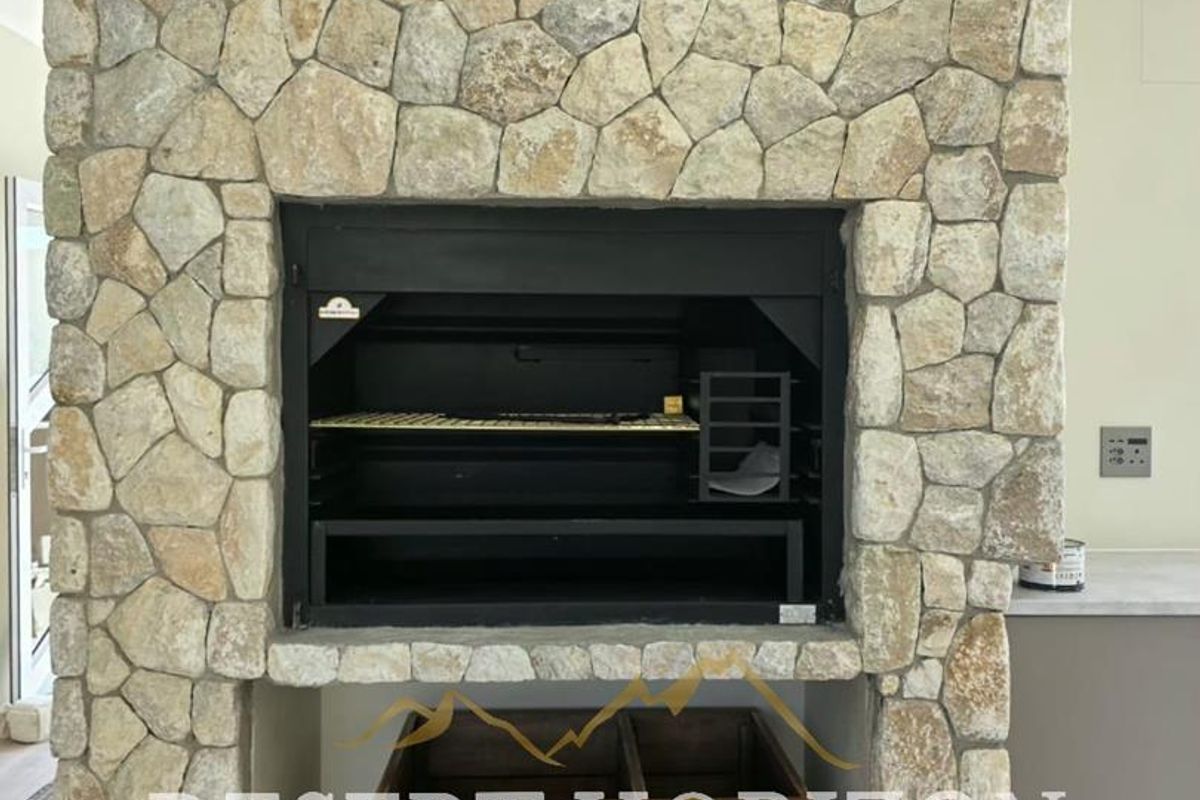 A feature stone fireplace with a built-in braai unit, set against a neutral interior with modern laminate flooring.
