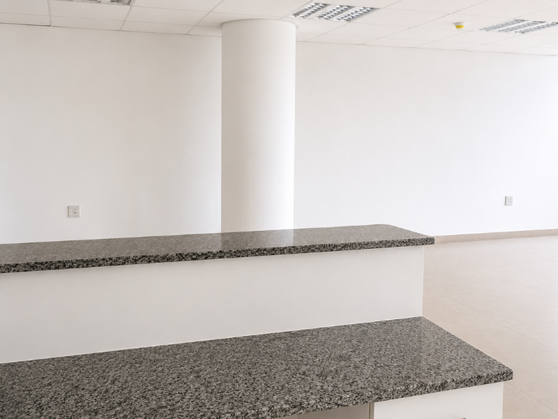 A clean, empty office space featuring a built-in granite reception desk, suspended ceiling with recessed lighting, and neutral tiled flooring.