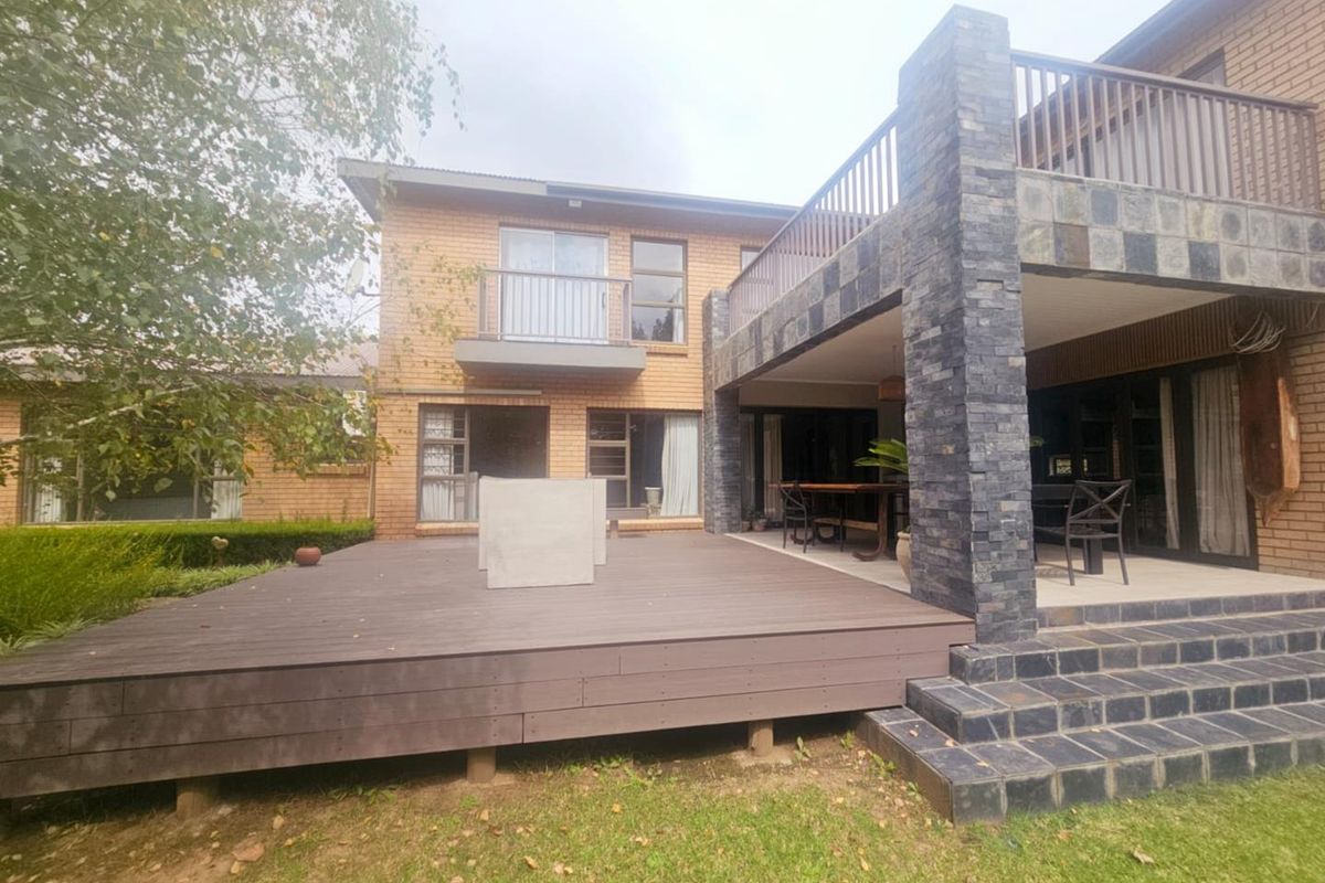 Spacious rear exterior featuring a raised timber deck, stone-clad patio area, and an upper-level balcony overlooking the garden.