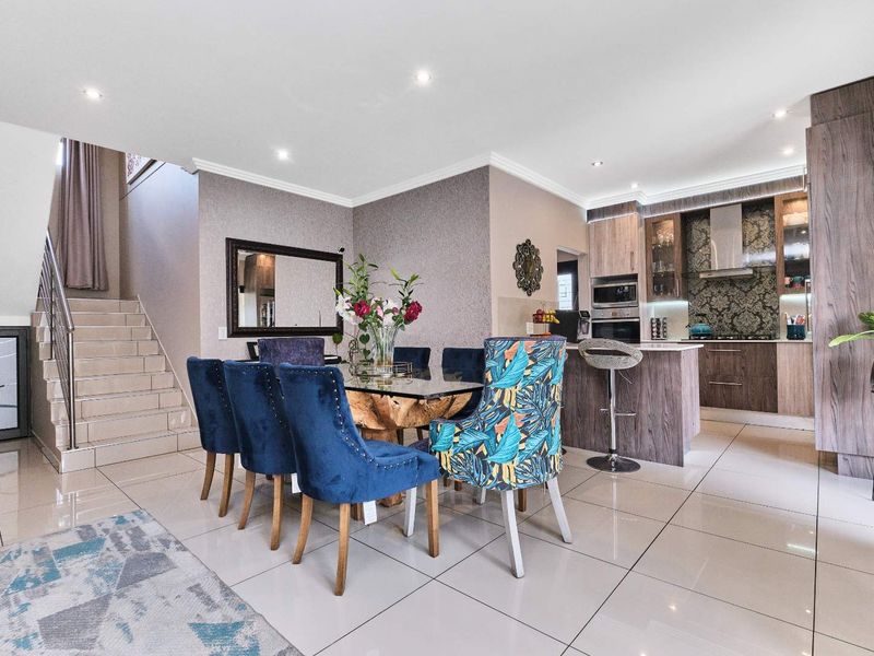 Modern open-plan living area featuring a dining space, a contemporary kitchen with built-in appliances, and a staircase with a sleek metal railing.