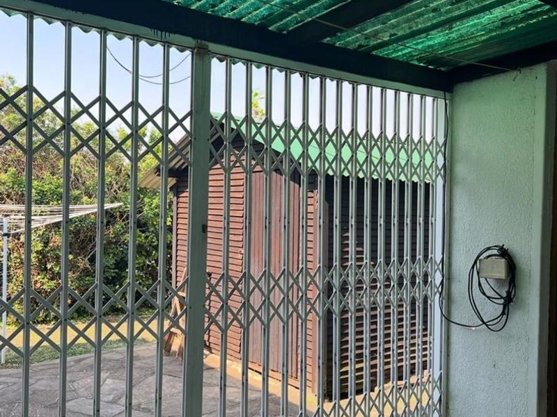 Covered patio area featuring a security gate, paved flooring, and an adjacent timber storage shed in the rear garden.