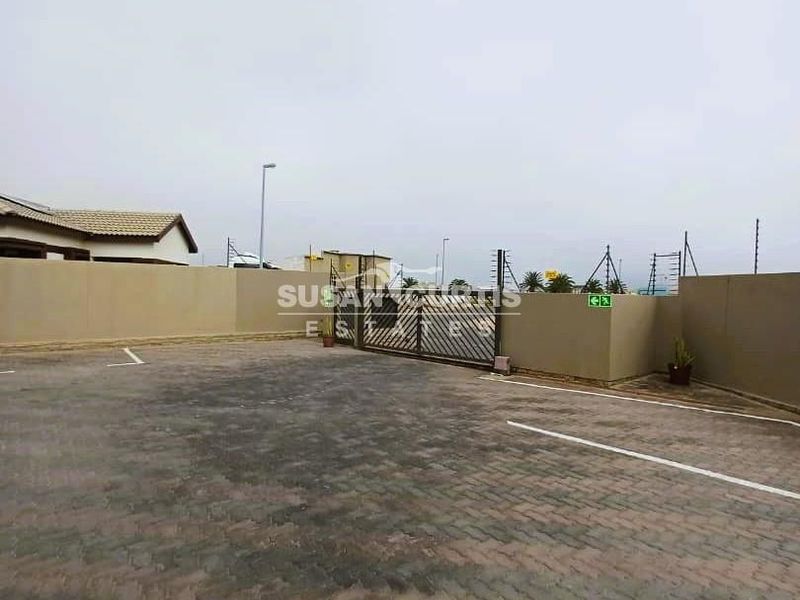 A paved front driveway and parking area featuring a secure sliding gate, perimeter walling, and electric fencing for enhanced property security.