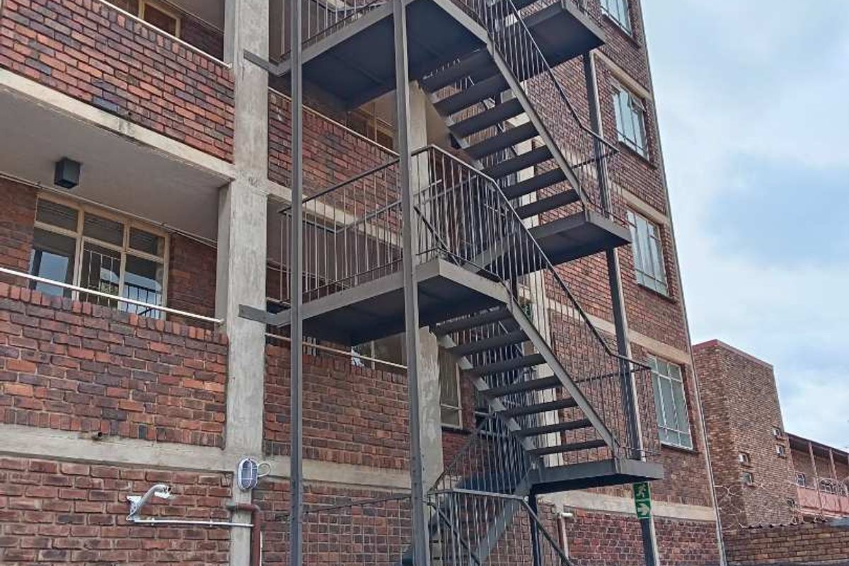 Exterior view of an apartment building featuring a multi-level steel fire escape staircase and traditional face brick facade.
