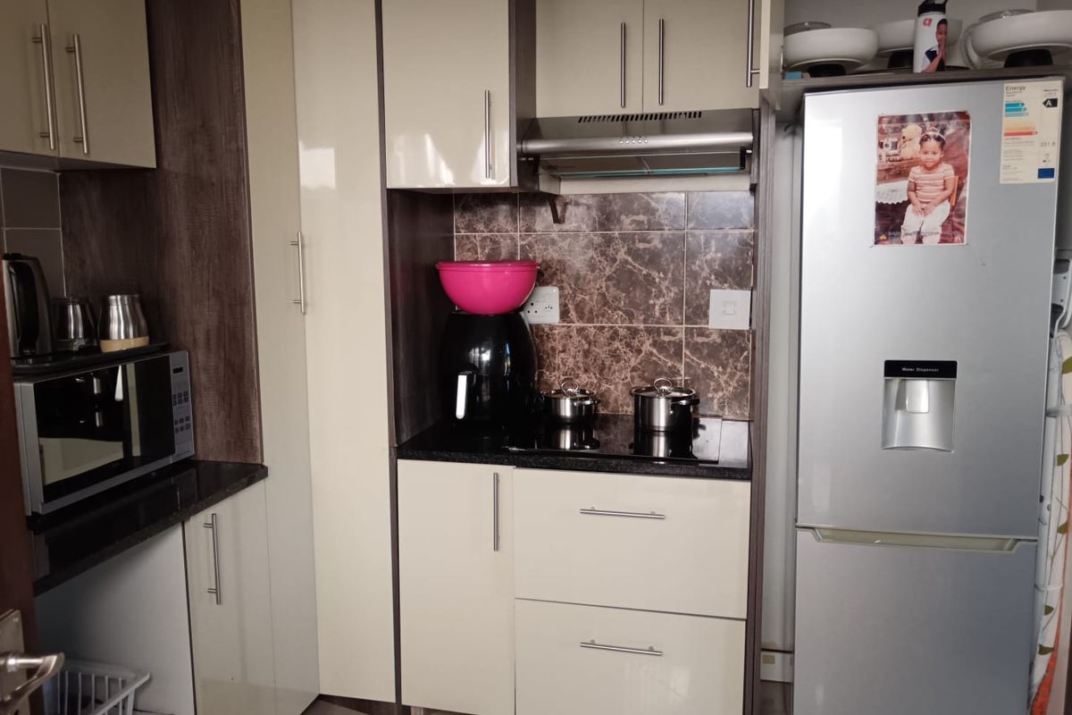 Compact modern kitchen featuring high-gloss cabinetry, granite countertops, a built-in electric hob with extractor fan, and a tiled backsplash.