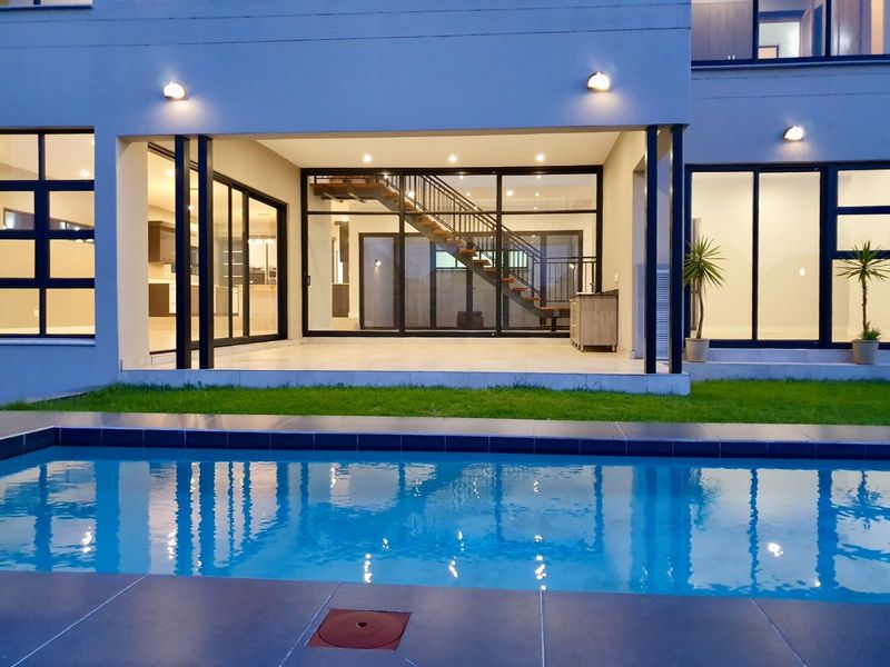 A modern rear exterior view featuring a swimming pool, a covered patio area, and large glass sliding doors leading into the home's interior.