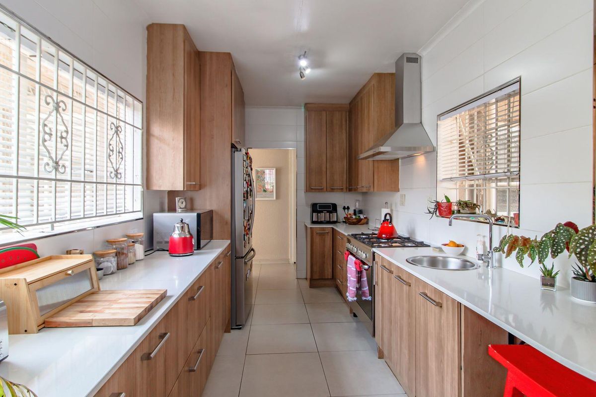 A functional galley-style kitchen featuring wood-finish cabinetry, stone countertops, a stainless steel extractor fan, and a gas hob.