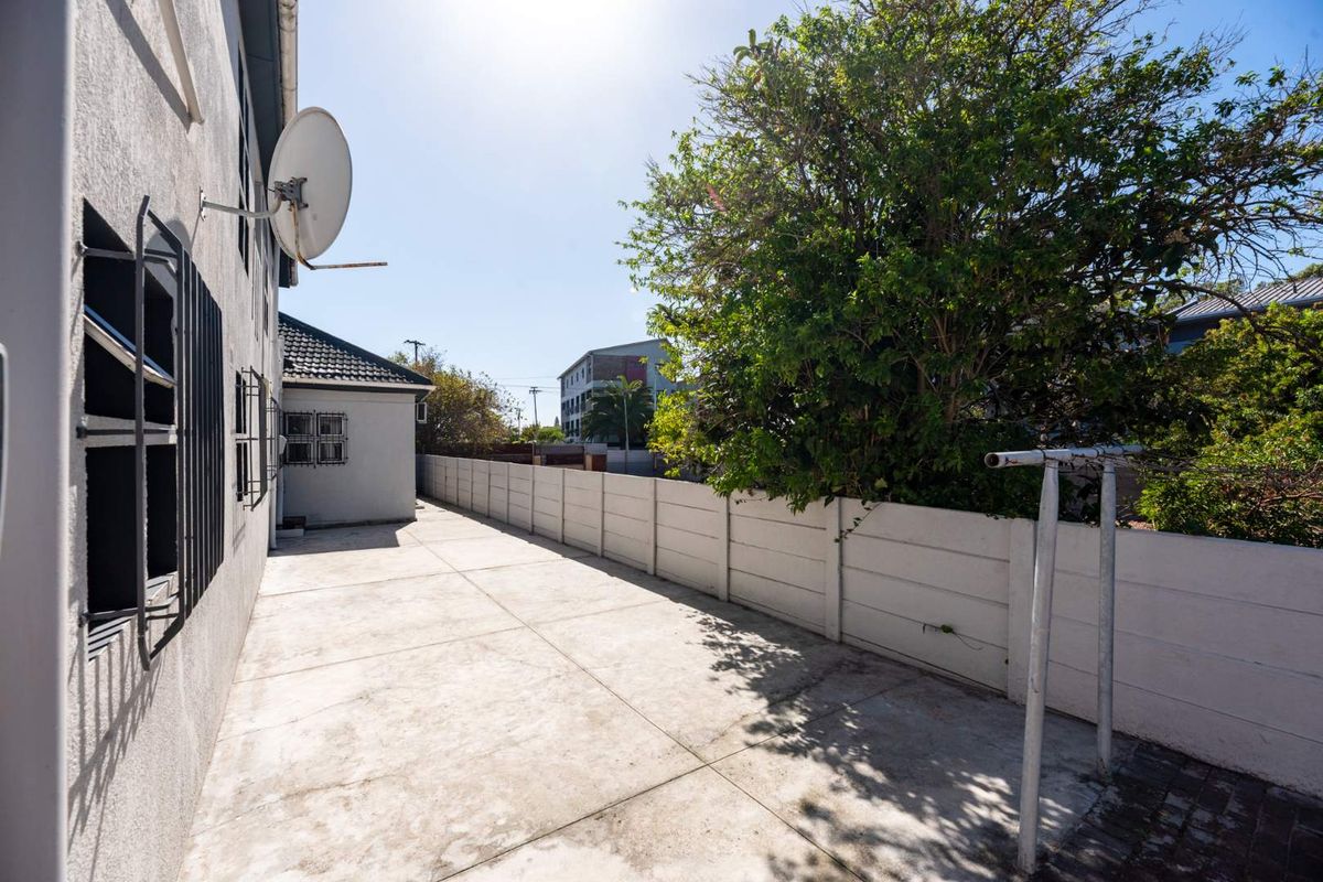 A paved rear exterior area featuring a concrete boundary wall, security bars on windows, and a satellite dish mounted to the building facade.