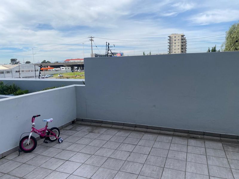 An open-air balcony featuring tiled flooring and a solid parapet wall, offering an elevated view of the surrounding urban landscape.