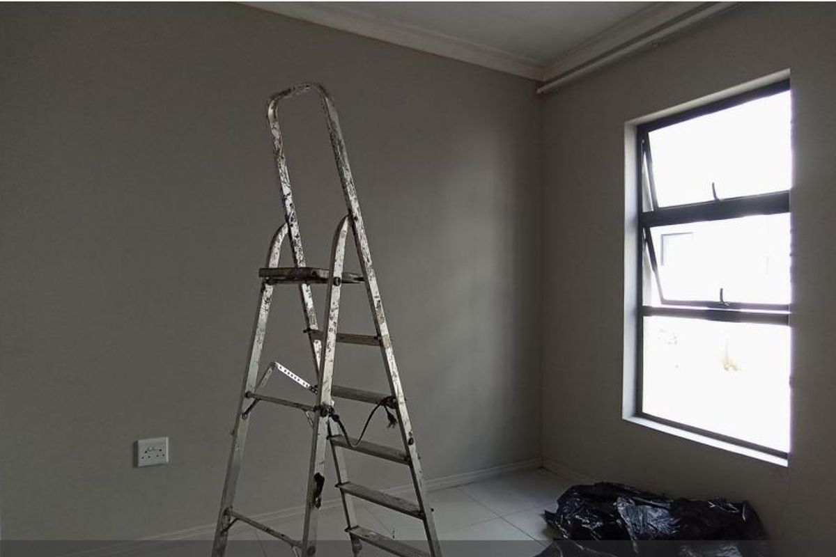 A neutral, empty bedroom featuring tiled flooring and a large window, currently undergoing minor maintenance or finishing work.