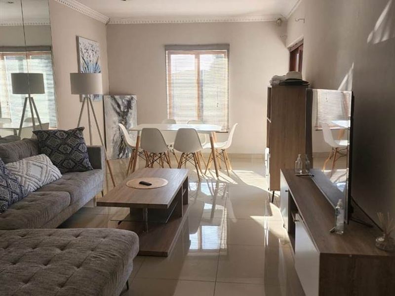 Spacious open-plan living and dining area featuring large format floor tiles, decorative crown molding, a ceiling fan, and a full-length mirrored wall.