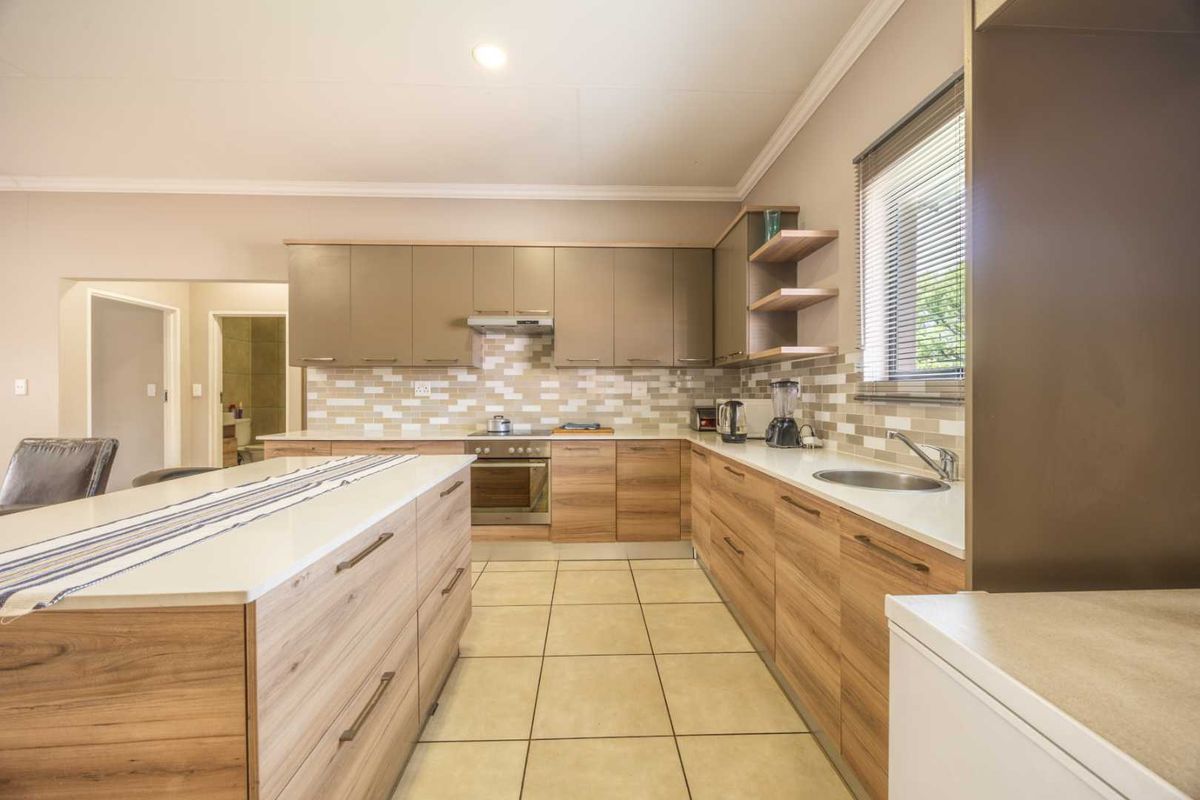 Modern kitchen featuring wood-finish cabinetry, a central island with stone countertops, built-in oven, extractor fan, and tiled flooring.