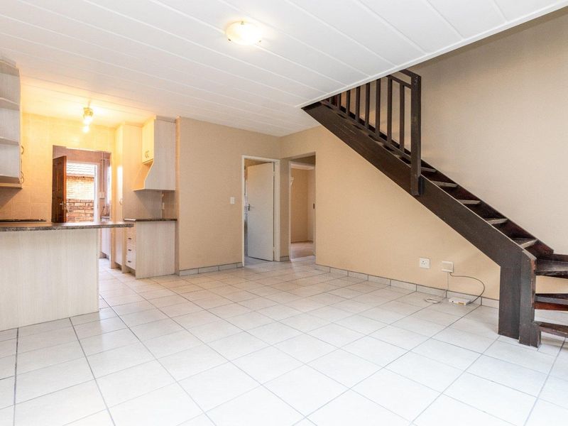 Open plan living area featuring tiled floors, a functional kitchen with built-in cabinetry, and a wooden staircase leading to the upper level.