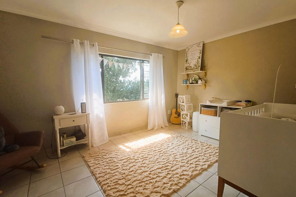 A bright bedroom featuring tiled flooring, neutral wall tones, and a large window providing natural light.