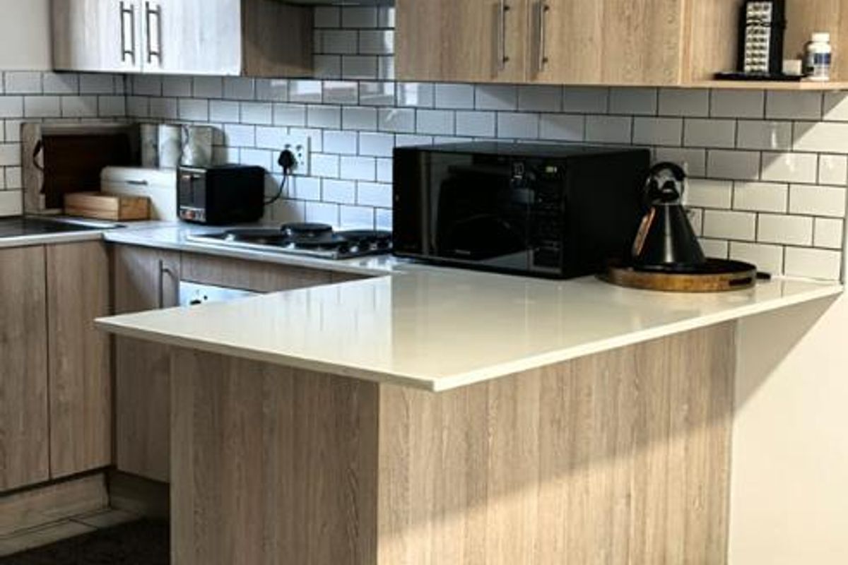 Modern kitchen featuring light wood-grain cabinetry, stone countertops, subway tile backsplash, and a functional breakfast bar layout.