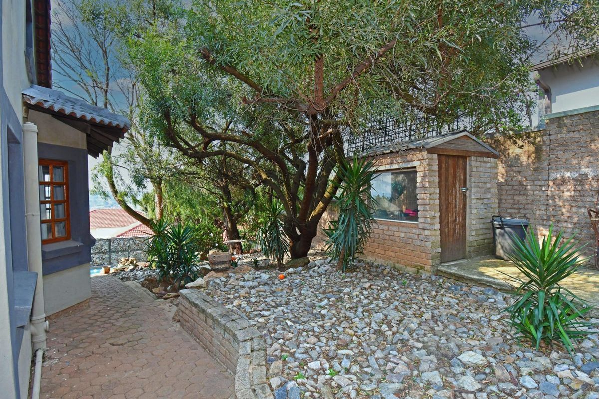 Rear garden area featuring a brick storage shed, paved walkway, and established trees with stone-covered landscaping.