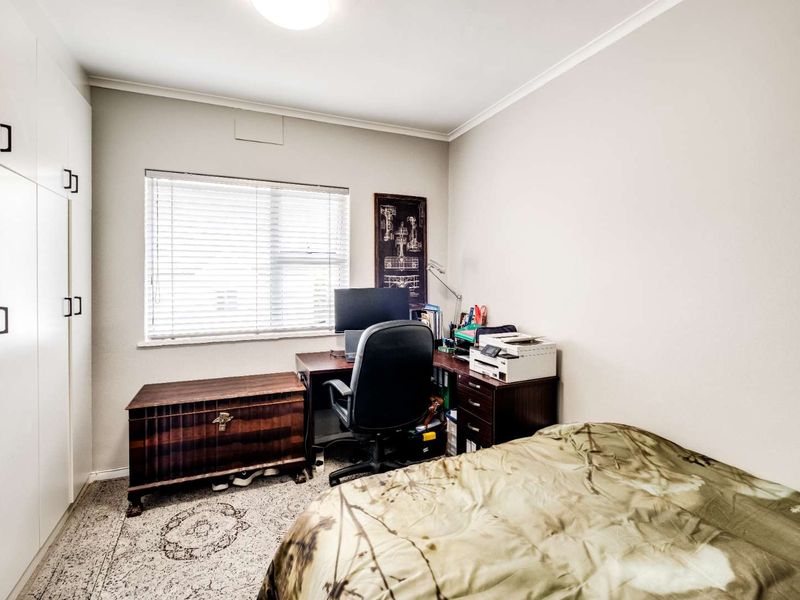 A functional bedroom featuring built-in cupboards, neutral wall finishes, and a window with venetian blinds, providing ample storage and natural light.