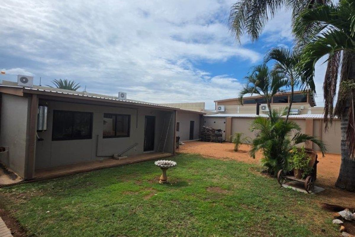 A spacious rear garden featuring a lawn area, paved walkway, and exterior access to the main dwelling with mounted air conditioning units.