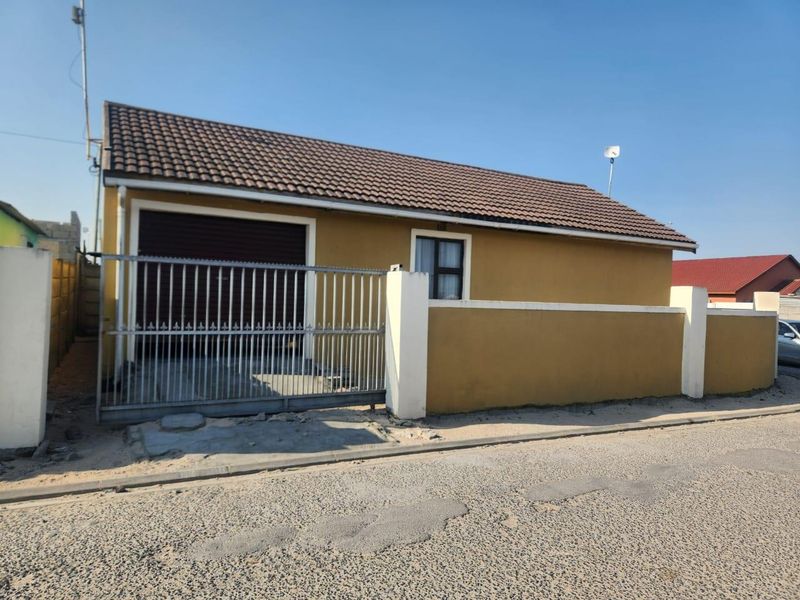 Front exterior view of a single-story house featuring a tiled roof, garage, and perimeter wall with a metal security gate.