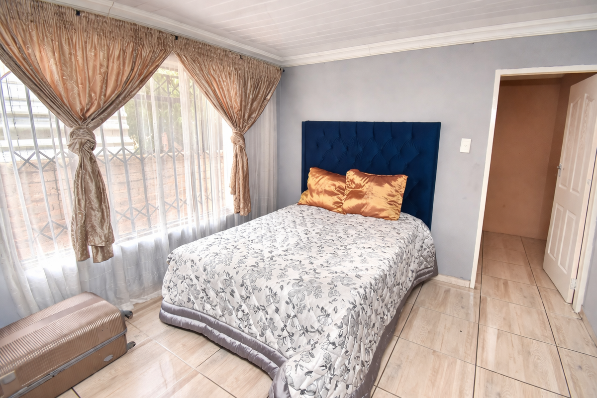 A bedroom featuring tiled flooring, a large window with security bars, and a neutral wall finish.
