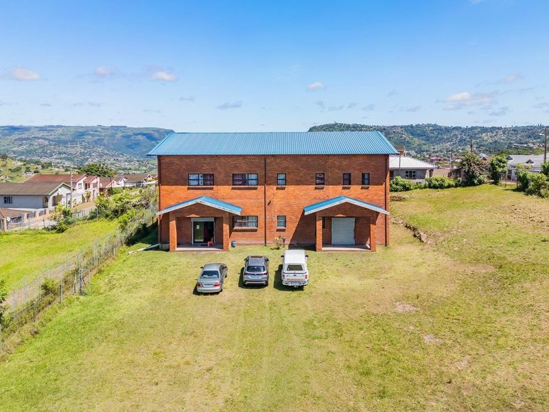 Aerial view of a two-story brick residential building with a metal roof, situated on a large plot of land with surrounding neighborhood views.