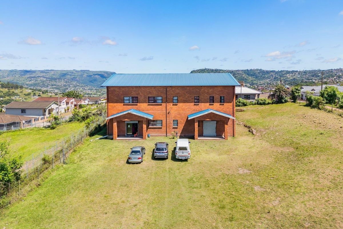 Aerial view of a two-story brick residential building with a metal roof, situated on a large plot of land with surrounding neighborhood views.