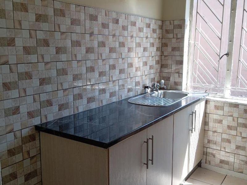 A compact kitchen area featuring built-in cabinetry, a dark laminate countertop with an integrated stainless steel sink, and decorative tiled splashbacks.