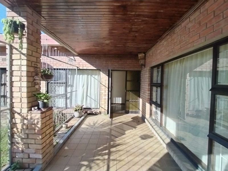 A covered outdoor patio featuring brick construction, a timber-paneled ceiling, and tiled flooring, providing a functional transition space between the interior and garden.