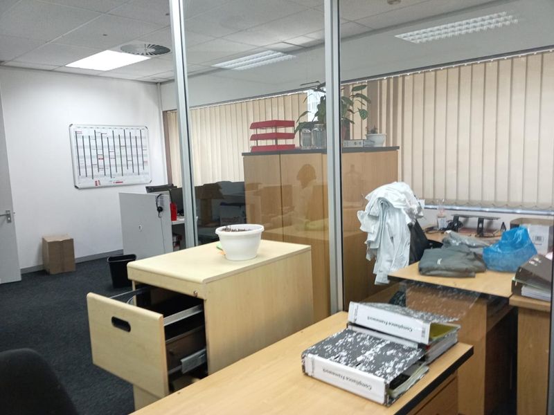A functional office space featuring glass partitioning, suspended ceilings with recessed lighting, and vertical blinds, providing a professional work environment.