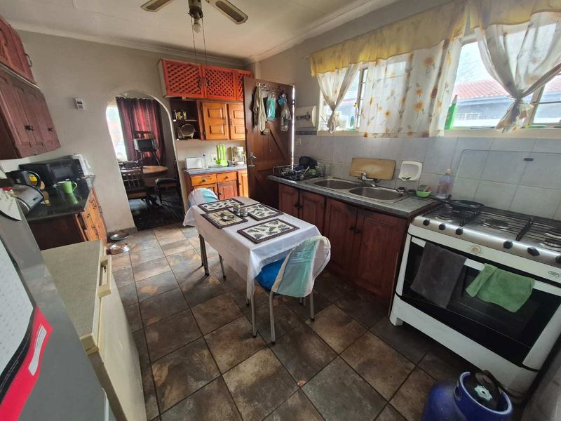 A dated kitchen featuring wooden cabinetry, a double basin sink, gas stove, and tiled flooring, with an archway leading to an adjacent dining area.